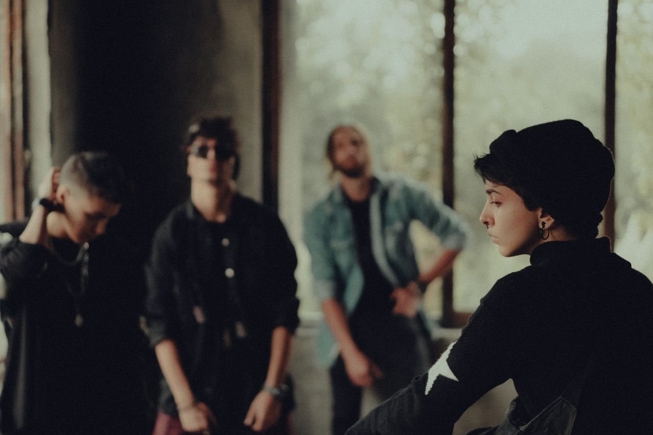 A fashionable group of young adults poses in a dimly lit room, evoking a sense of mystery.