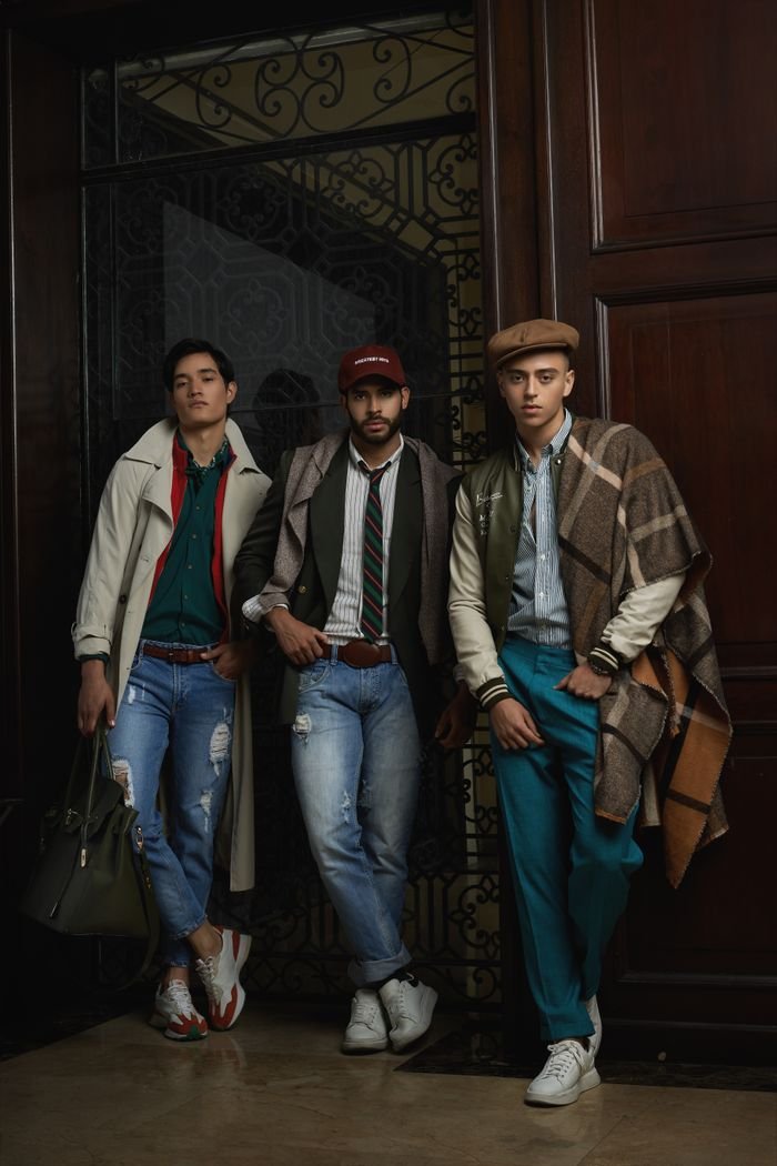Three stylish men pose indoors in trendy casual attire, highlighting modern fashion trends.