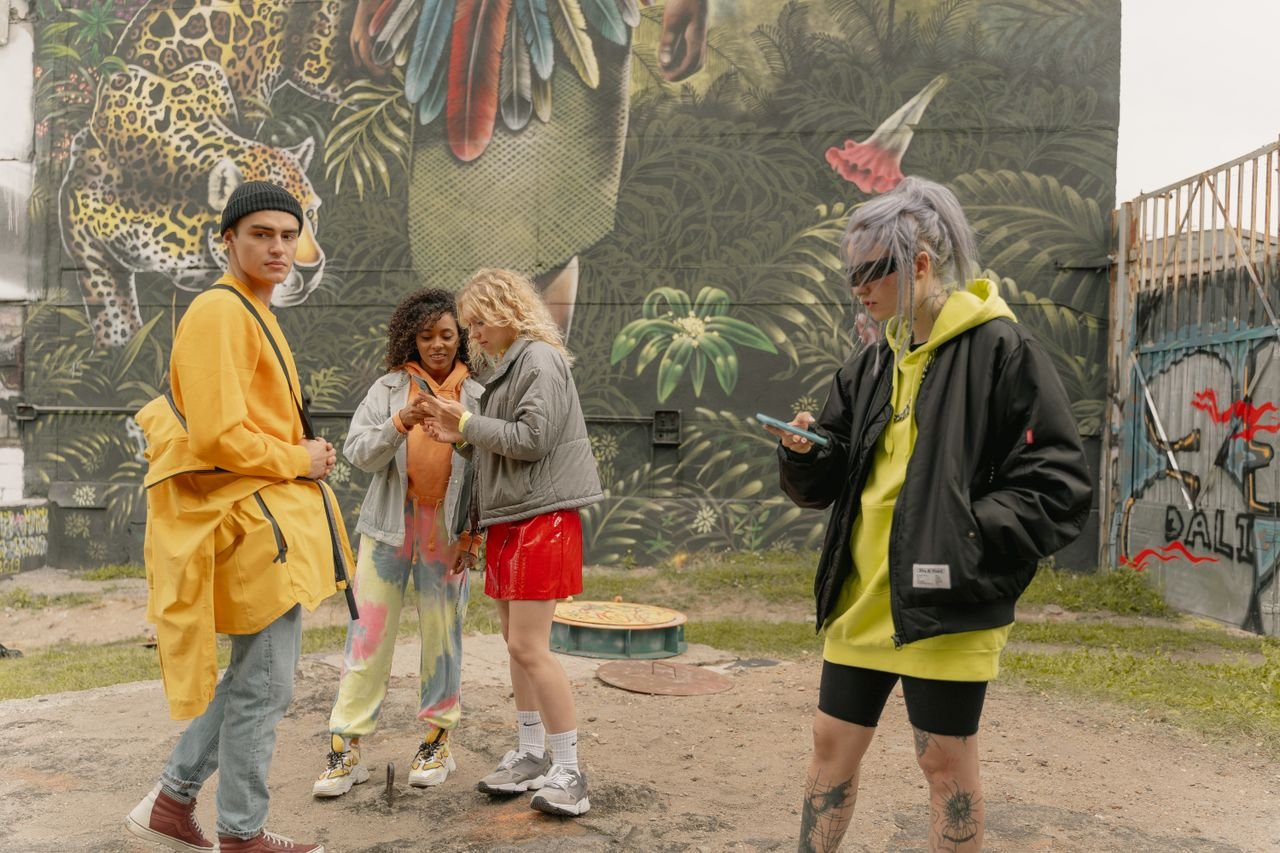 A group of diverse friends in stylish streetwear hang out by graffiti art outdoors.